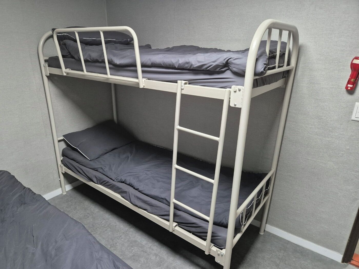 A bunk bed with grey bedding in a room with grey walls and a grey carpet.