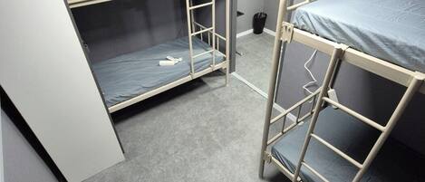 Una habitación con literas, una puerta y un cubo de basura.