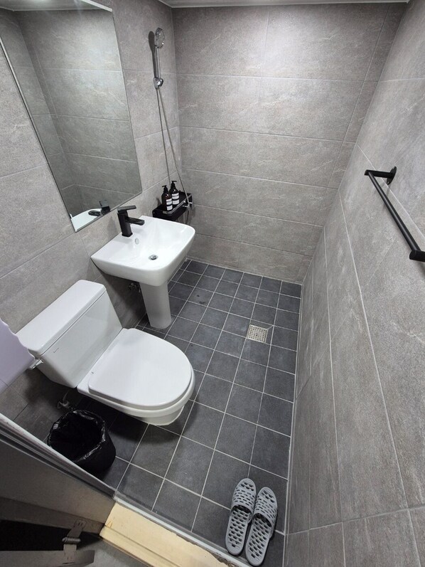 Un baño pequeño y moderno con inodoro, lavabo y ducha. Hay un espejo sobre el lavabo y un estante con artículos de aseo.