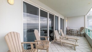 A balcony with several Adirondack chairs, a small table, and a view of the ocean through large glass doors. - Silver Beach 206 by Liquid Life (Orange Beach)
