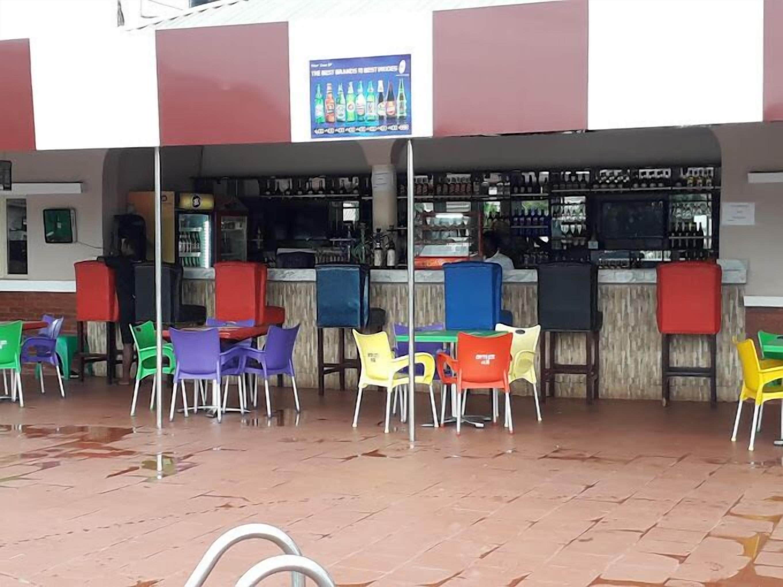 An outdoor seating area with colorful plastic chairs and tables, a bar area with shelves of bottles, and a sign advertising the best drinks.