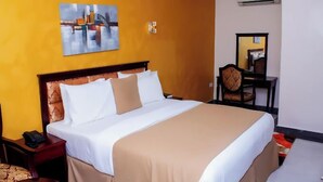 A hotel room with a large bed, a bedside table with a phone, a chair, and a mirror. - Crown City Resorts  (Agbara)