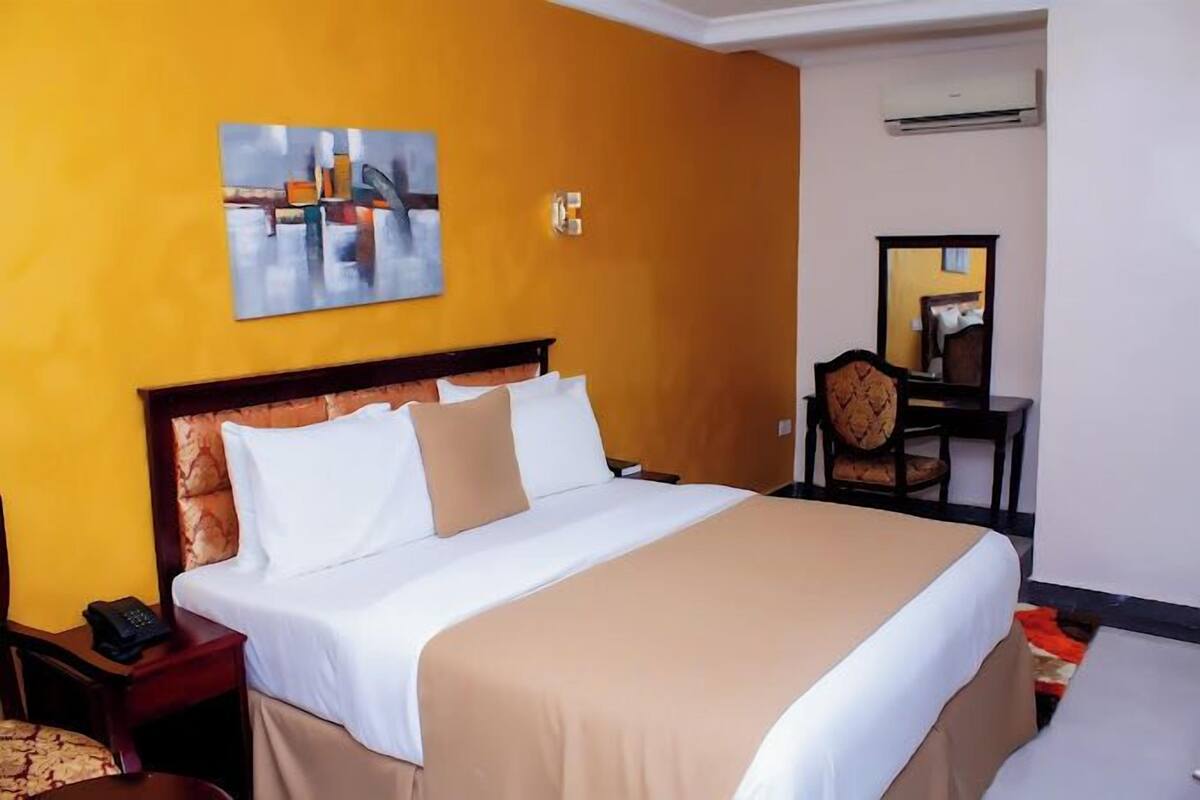 Une chambre d’hôtel avec un grand lit, une table de chevet avec un téléphone, une chaise et un miroir.