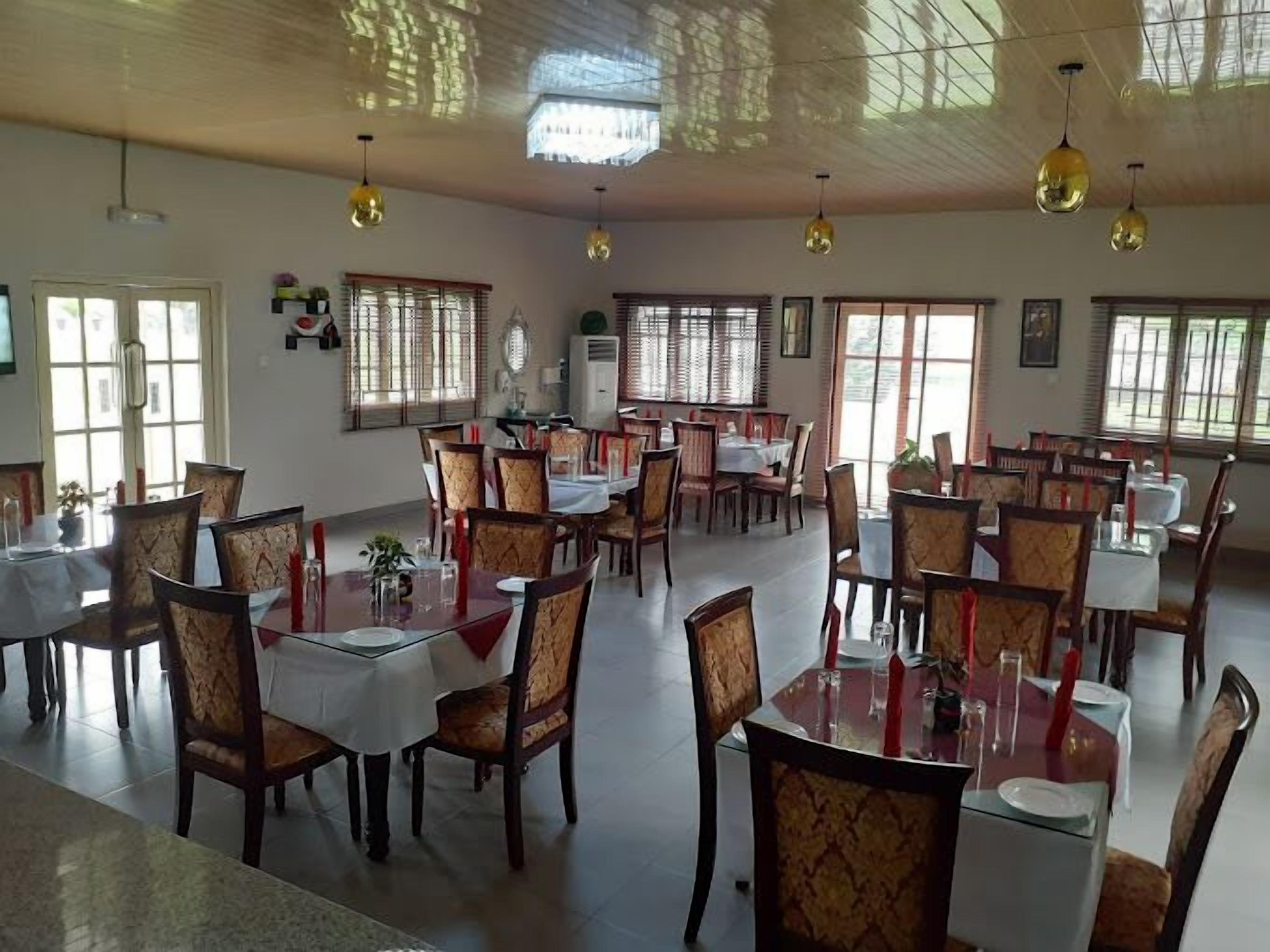 A spacious dining area with multiple tables and chairs, large windows allowing natural light, and hanging pendant lights.