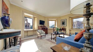 A spacious living room with a large window, a blue sofa, a wooden coffee table, and a decorative lamp. - Colosseo Way (Roma)