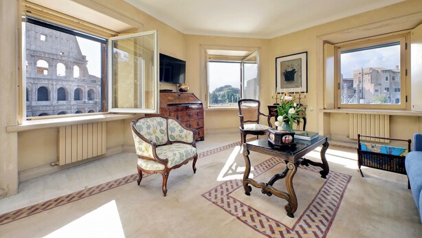 A spacious living room with large windows offering views of a historic building. - Colosseo Way (Roma)