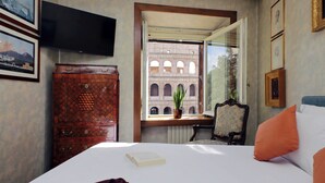 A hotel room with a bed, a television mounted on the wall, a wooden cabinet, and a window with a view of a building. - Colosseo Way (Roma)