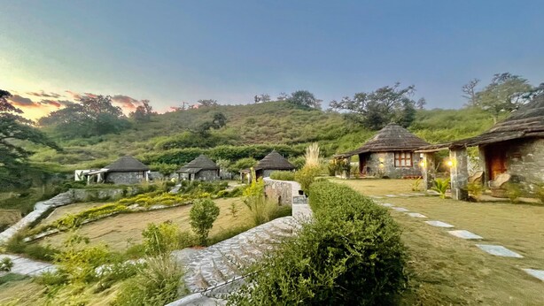 A rural village with traditional thatched-roof houses, stone pathways, and lush greenery. - Turban Nature Wilderness Kumbhalgarh  (Gogunda)