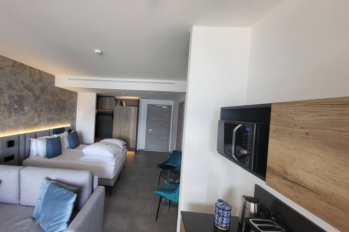 Een moderne hotelkamer met een bank, twee bedden, een televisie en een kitchenette.