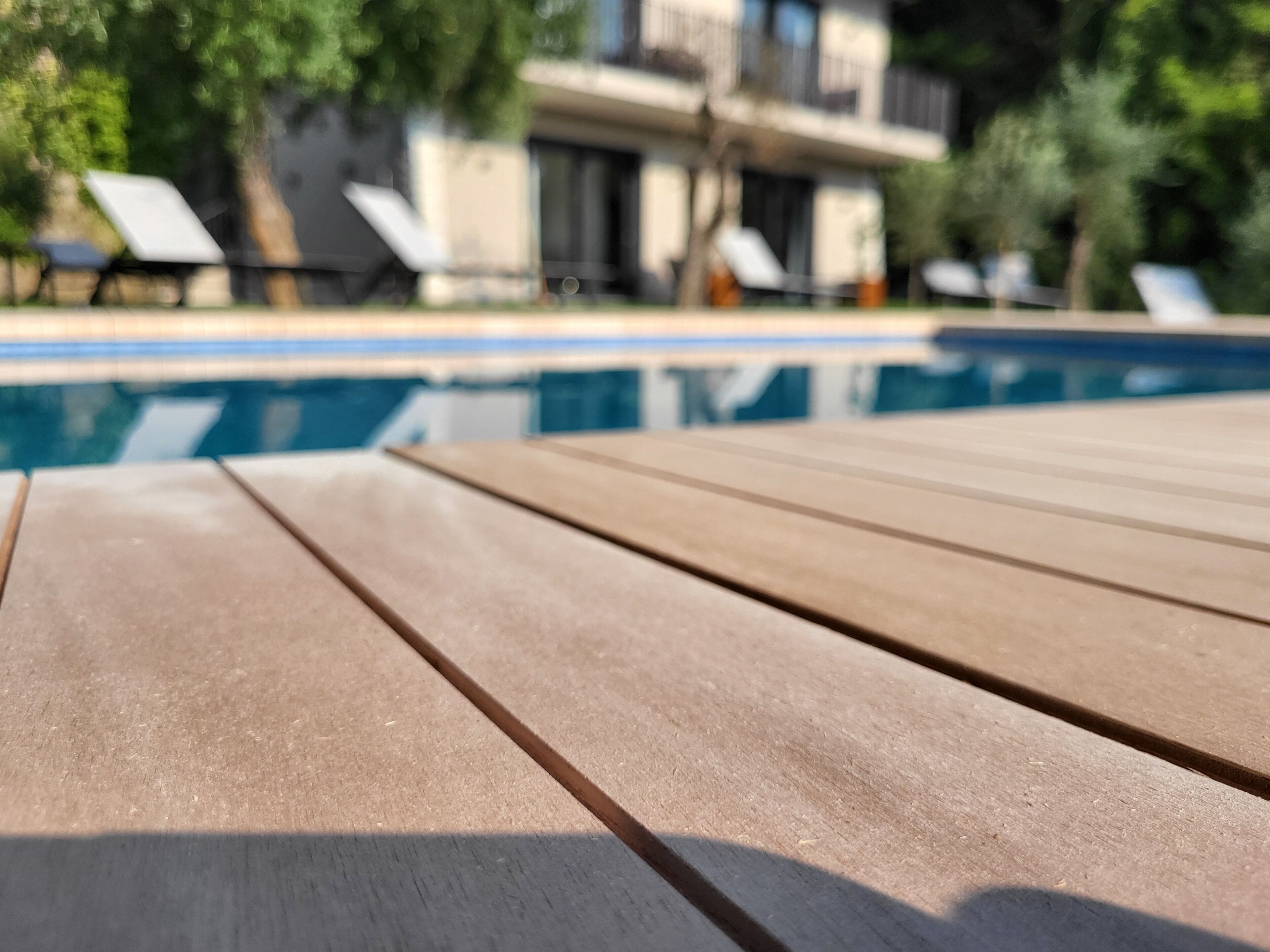 A wooden poolside table with a clear view of a swimming pool and lounge chairs in the background.
