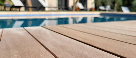 A wooden poolside table with a clear view of a swimming pool and lounge chairs in the background.