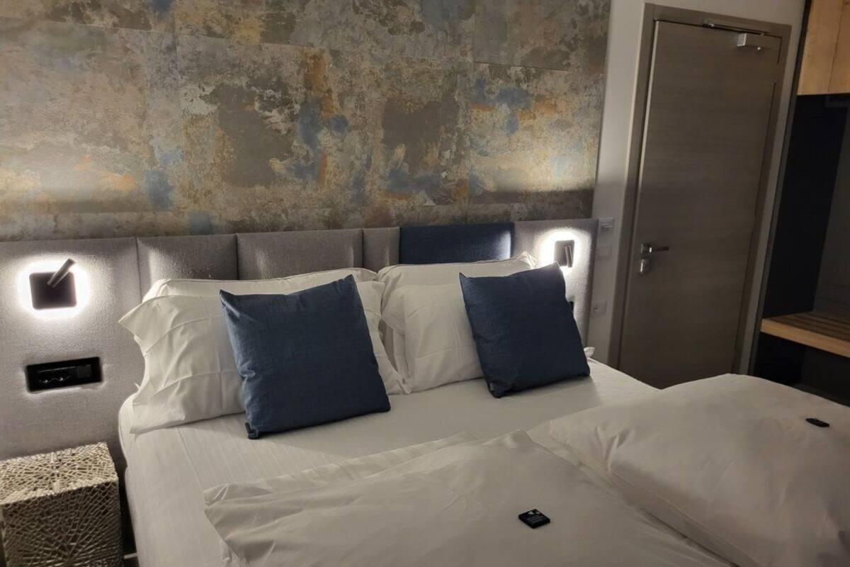 Een bed met witte lakens en blauwe kussens, een gestructureerde muur achtergrond en een deur aan de rechterkant.