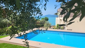 A swimming pool with a wooden deck, surrounded by greenery and a view of the sea. - Attilio High Living Suites - Adults Only (Torri del Benaco)