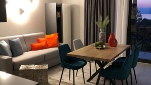 A modern living room with a sofa, teal chairs, a wooden dining table, and a view of the outdoors. - Attilio High Living Suites - Adults Only (Torri del Benaco)