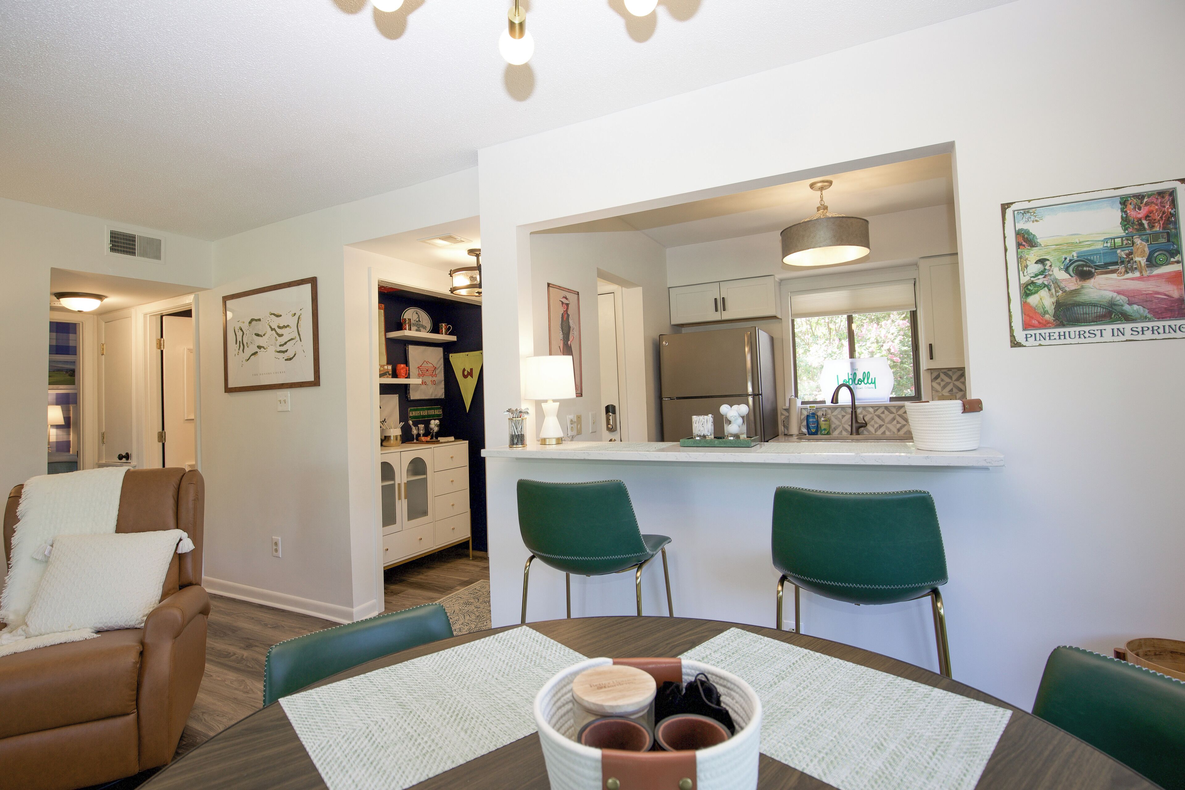 Une cuisine moderne équipée d’un réfrigérateur, un coin repas avec une table et des chaises, et un salon avec un canapé et une lampe.