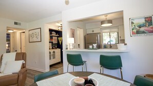 Eine moderne Küche mit Kühlschrank, ein Essbereich mit Tisch und Stühlen sowie ein Wohnzimmer mit Sofa und Lampe.