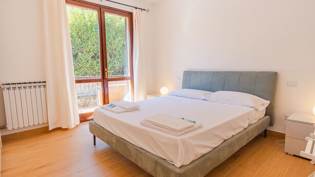 Ein Schlafzimmer mit einem Bett, einem Nachttisch, einem Fenster mit Vorhängen und einer Heizung.