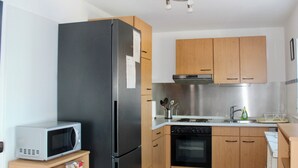 Une cuisine compacte équipée d’un réfrigérateur, d’un four à micro-ondes, d’un four traditionnel et de meubles de rangement en bois.
