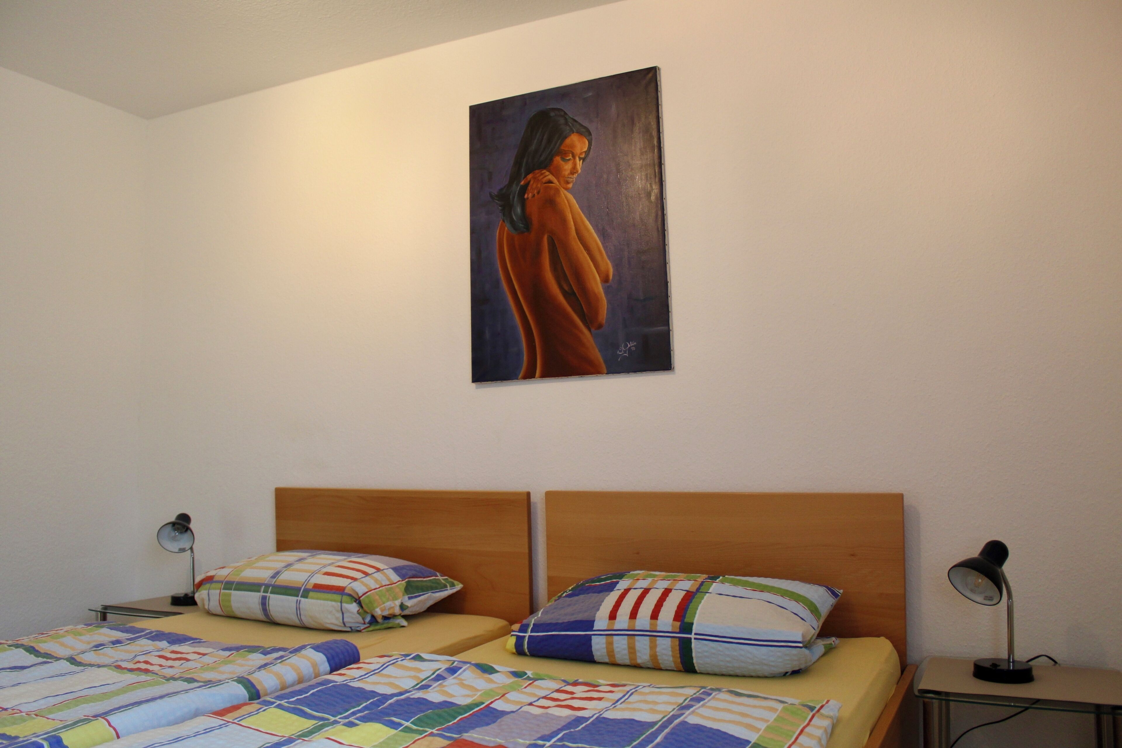 Une chambre avec deux lits, chacun agrémenté d’une couverture colorée et d’oreillers à rayures. Un tableau est accroché au mur, au-dessus des lits.