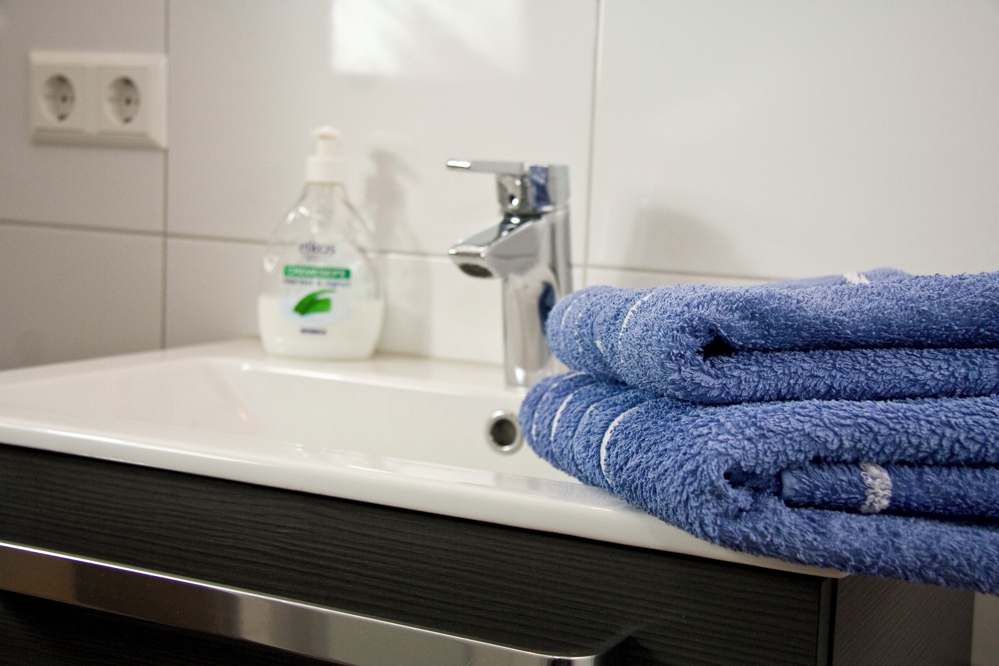 A bathroom sink with a bottle of hand soap and a folded blue towel.
