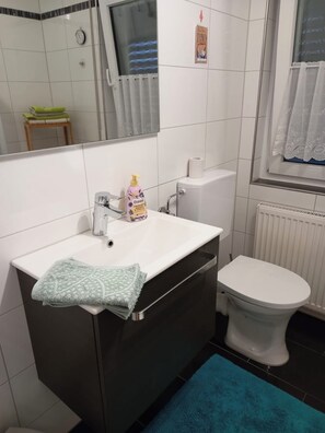 Un bagno con un lavandino bianco, uno specchio, un water e un tappetino da bagno blu.