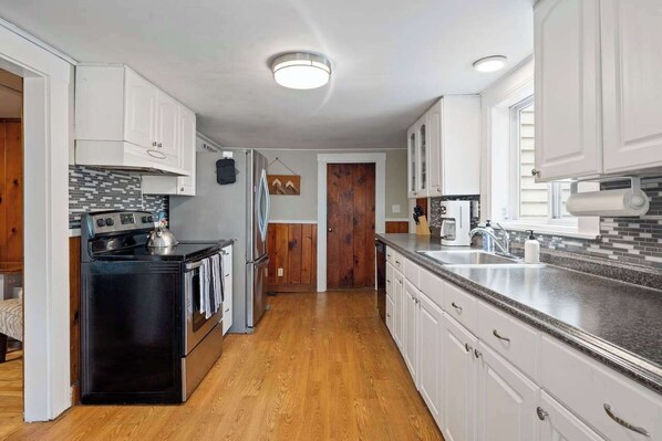 A modern kitchen with white cabinets, a black stove, and a wooden floor.