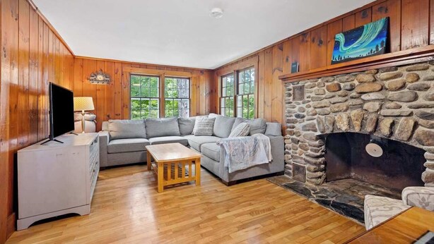 Ein gemütliches Wohnzimmer mit Kamin aus Stein, Holzwänden und einem grauen Sofa.
