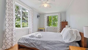 Ein Schlafzimmer mit einem Bett, einem Deckenventilator und Fenstern mit Vorhängen.