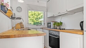 A kitchen with a wooden countertop, white cabinets, a microwave, an oven, and a window with a view of trees.