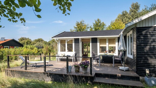 A wooden deck with outdoor seating and a covered area, surrounded by greenery and a house.