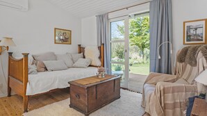 A cozy bedroom with a bed, a wooden chest, a chair, and a large window with curtains.