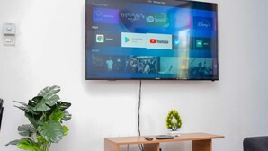 A flat-screen TV mounted on a white wall, displaying a streaming app interface. - Casey's Apartments Bamburi (Mombasa)