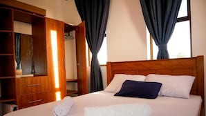 A neatly made bed with white and navy pillows, a rolled white towel, and a wooden headboard. - Casey's Apartments Bamburi (Mombasa)