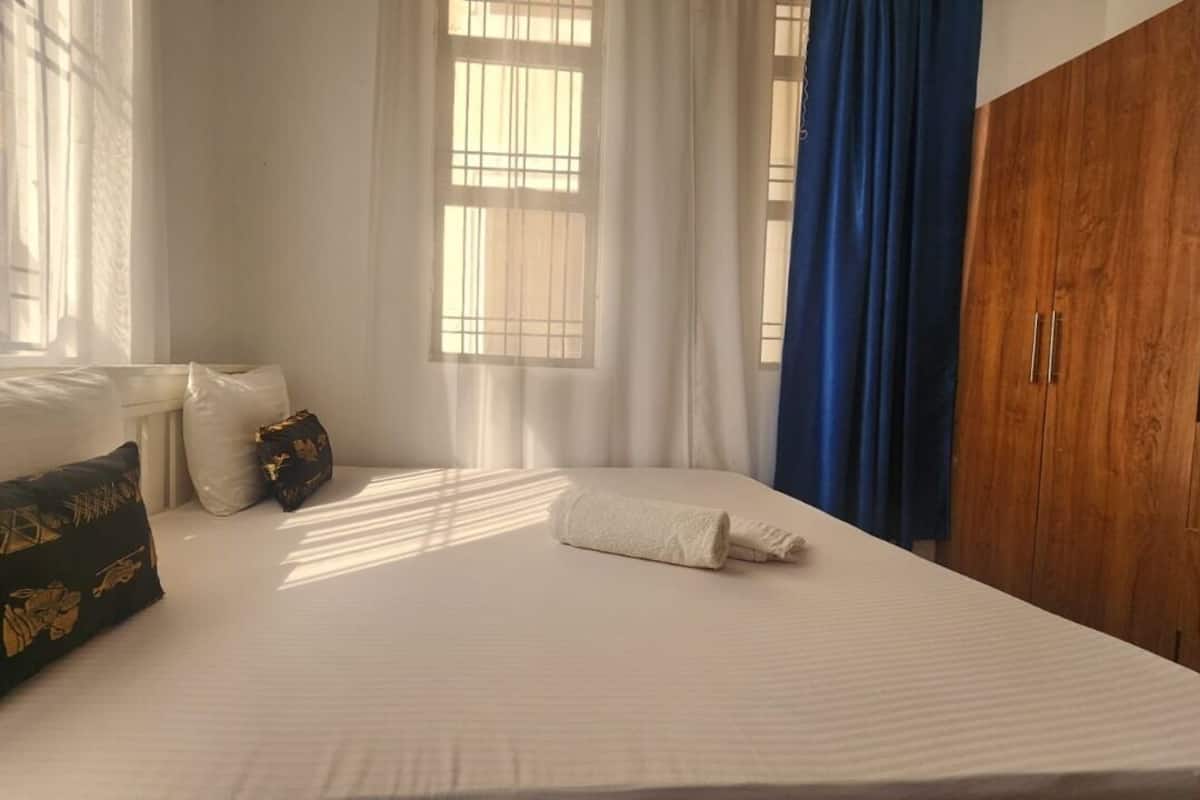 Ein Schlafzimmer mit einem Bett, Kissen, einem Holzschrank und einem Fenster mit Vorhängen.