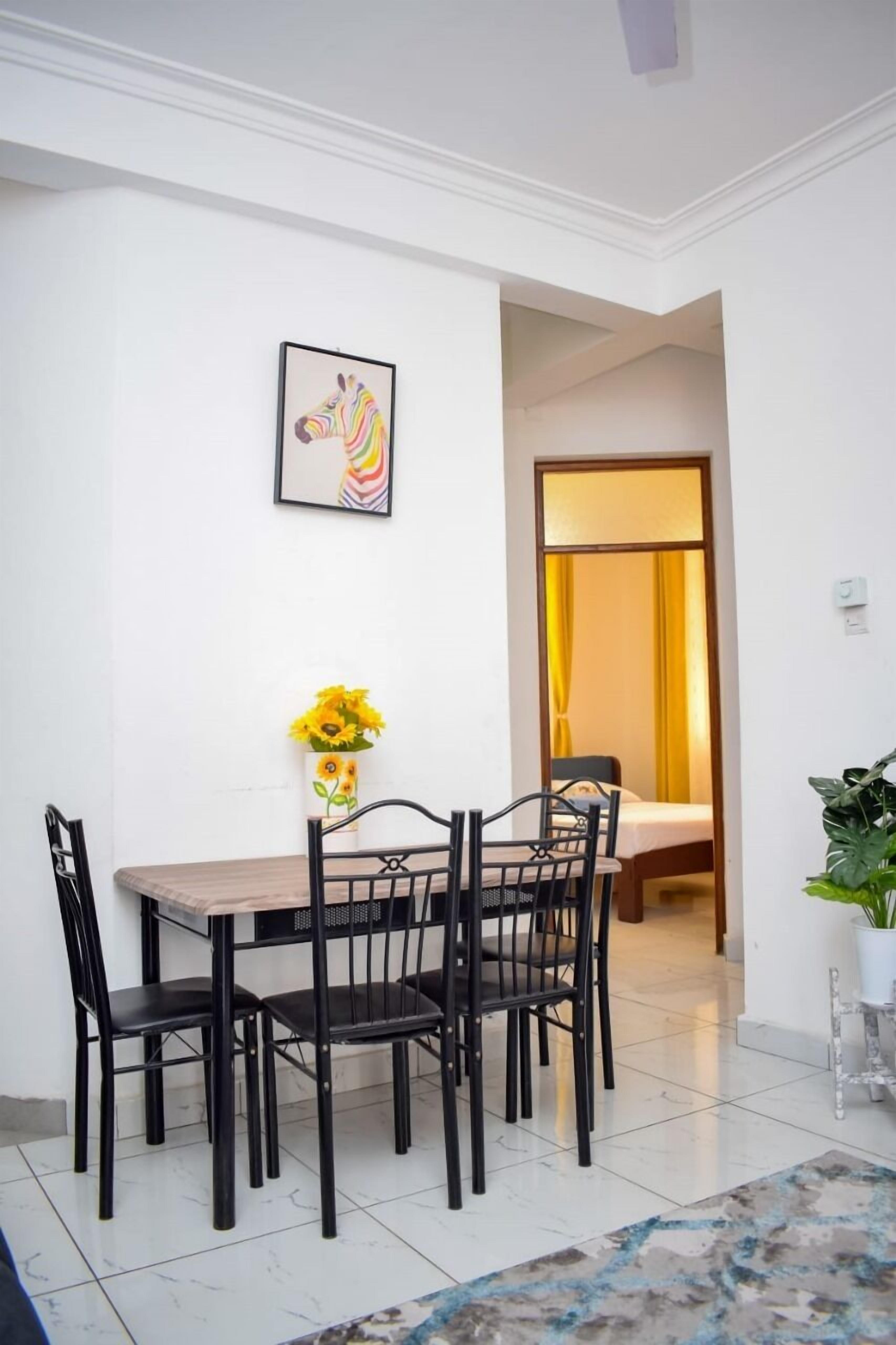 A dining area with a table and chairs, a framed artwork on the wall, and a vase with sunflowers.
