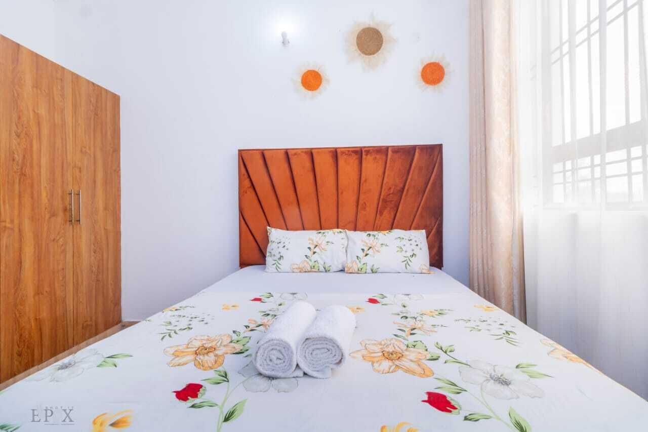 A bedroom with a wooden wardrobe, a bed with floral bedding, and a sun decoration on the wall.