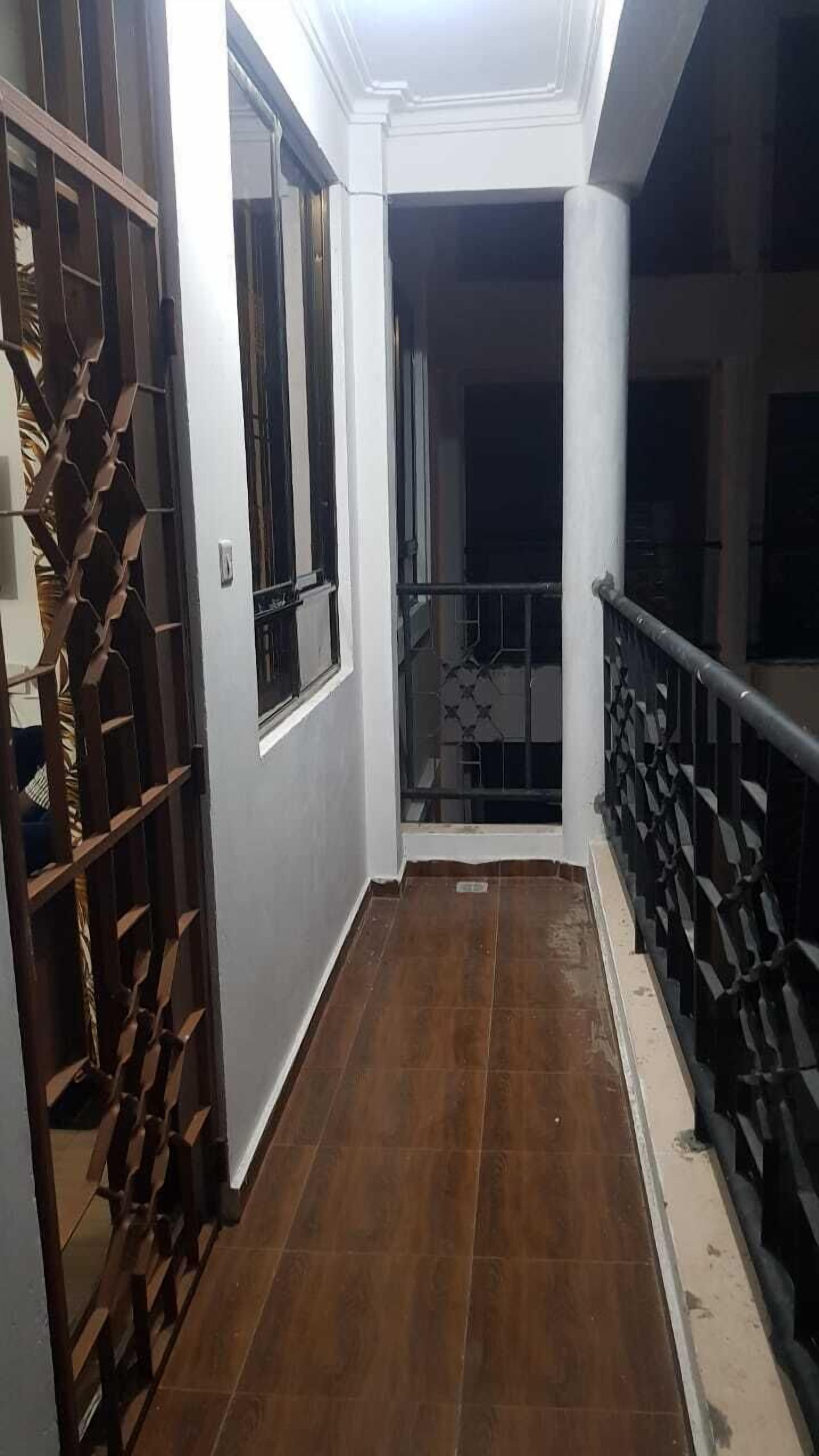 Een gang met een houten vloer, witte muren en een metalen poort aan de linkerkant.