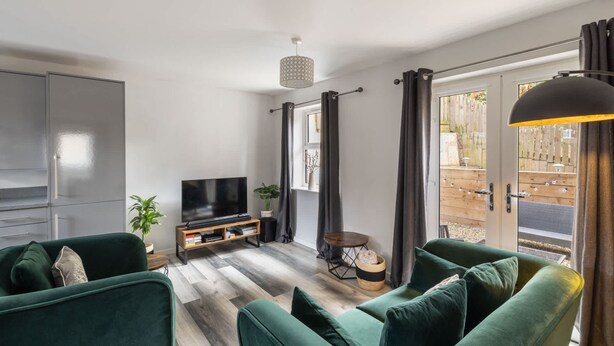 Una sala de estar moderna con un sofá verde, un televisor de pantalla plana y piso de madera.