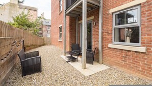 Edificio de ladrillo con un patio que tiene muebles de exterior y una valla de madera.
