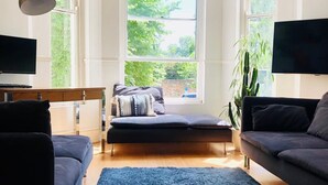 Un salon moderne avec un tapis bleu foncé, deux canapés, un banc et un téléviseur posé sur un meuble.