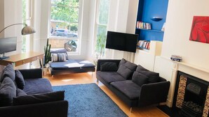 Un salon moderne comprenant un canapé, une table basse, un téléviseur à écran plat, une bibliothèque et une cheminée.