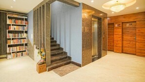 Eine moderne Hotellobby mit einer Marmortreppe, einem Holzbüro und einem Bücherregal voller Bücher.