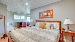 A bedroom with a large bed, a wooden headboard, a nightstand with a lamp, a wooden dresser, a window, and a ceiling fan. - 'Holmes With a View' Studio: Millersburg Retreat! (Millersburg)