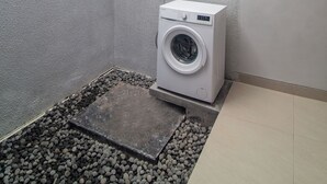 A compact, modern bathroom with a built-in washing machine, a small window, and a tiled floor. - Casa de la Vida (Tabanan)