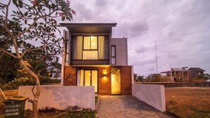 A modern two-story house with a brick facade, large windows, and a paved driveway. - Casa de la Vida (Tabanan)