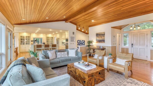 Ein geräumiges Wohnzimmer mit Holzboden, einem grauen Sofa, einem Holztisch und Blick in den Küchenbereich.