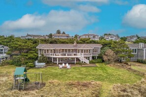 A large two-story house with a covered porch, a small play area, and a well-maintained lawn. - Elk Ridge -  Lux Oceanfront Home, Hot Tub & Games (Seaside)