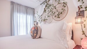 A bedroom with a large bed, a bedside table with a lamp, and a wall decorated with macramé and greenery.