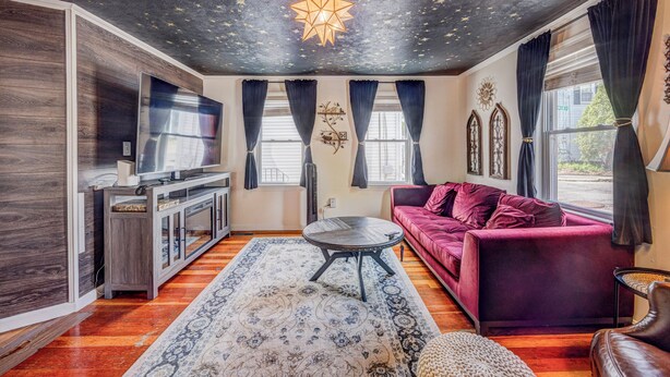 A living room with a starry ceiling, a large TV, a red sofa, and a wooden floor.