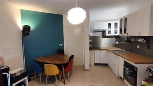 Une cuisine compacte avec un coin repas, des meubles blancs, un plan de travail en bois et un mur d’accent bleu.